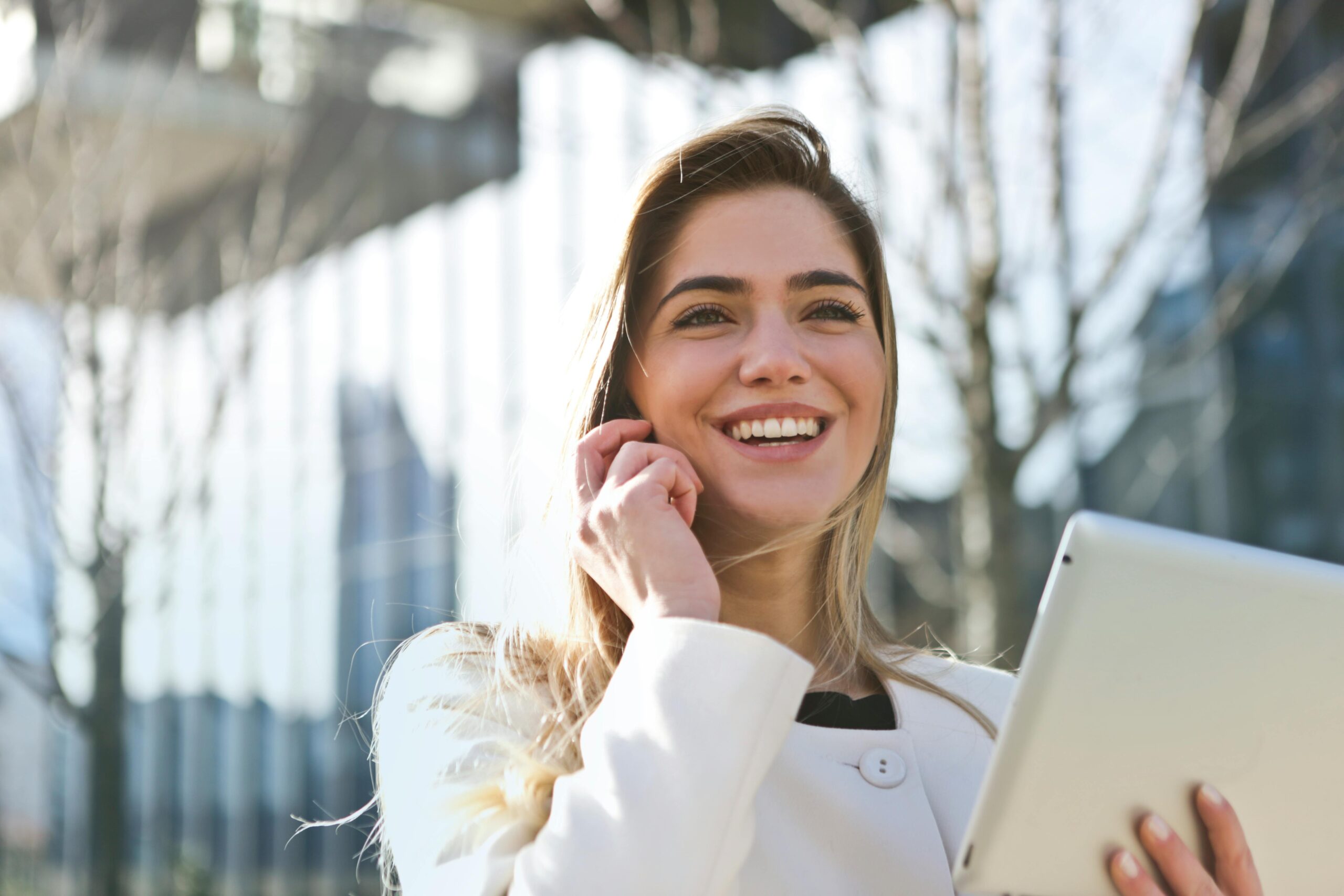 A smiling woman multitasks with a phone call and a tablet in hand, representing the ease of handling UBO compliance digitally and efficiently.